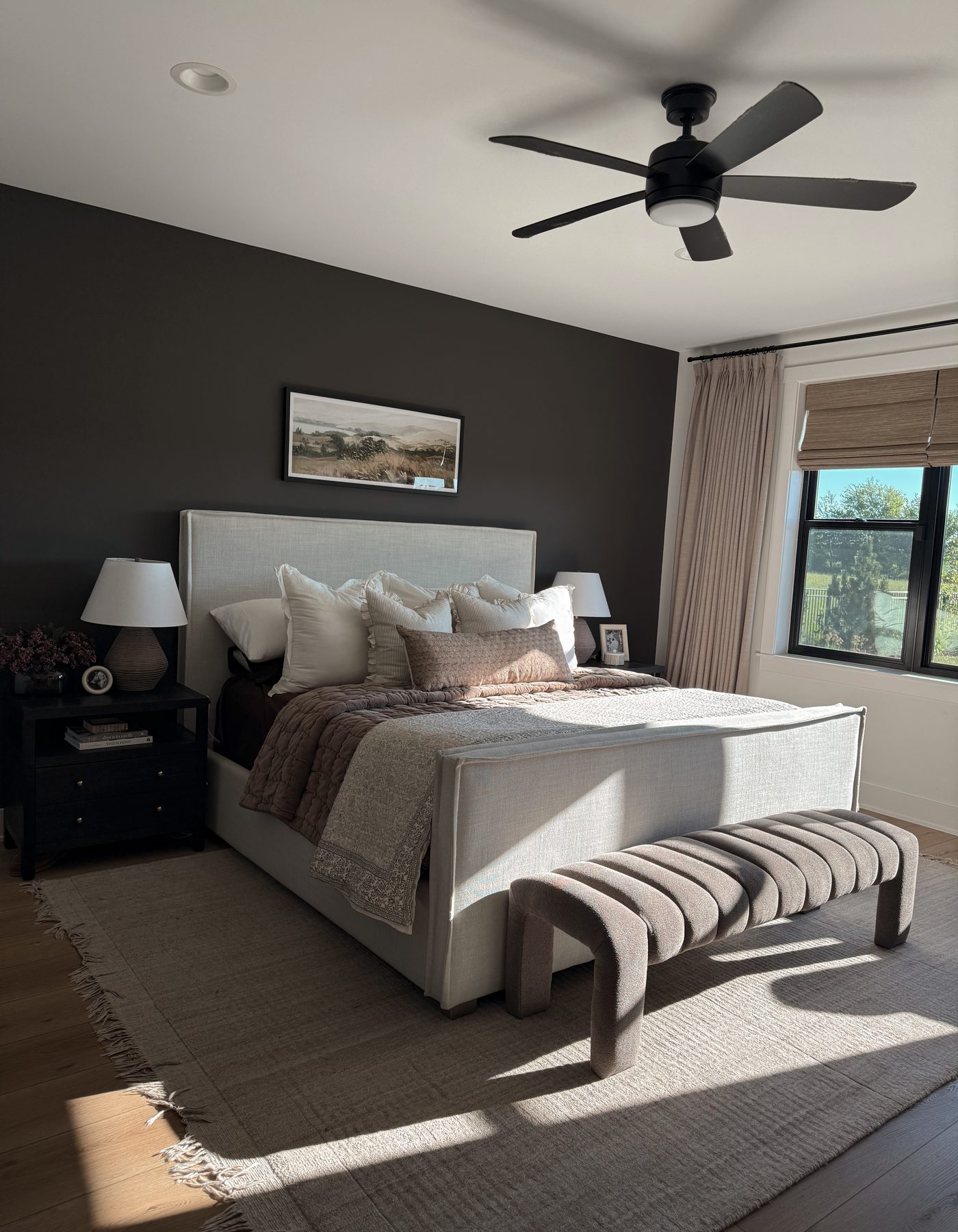 A primary bedroom with a linen bed, dark accent wall, and layered bedding